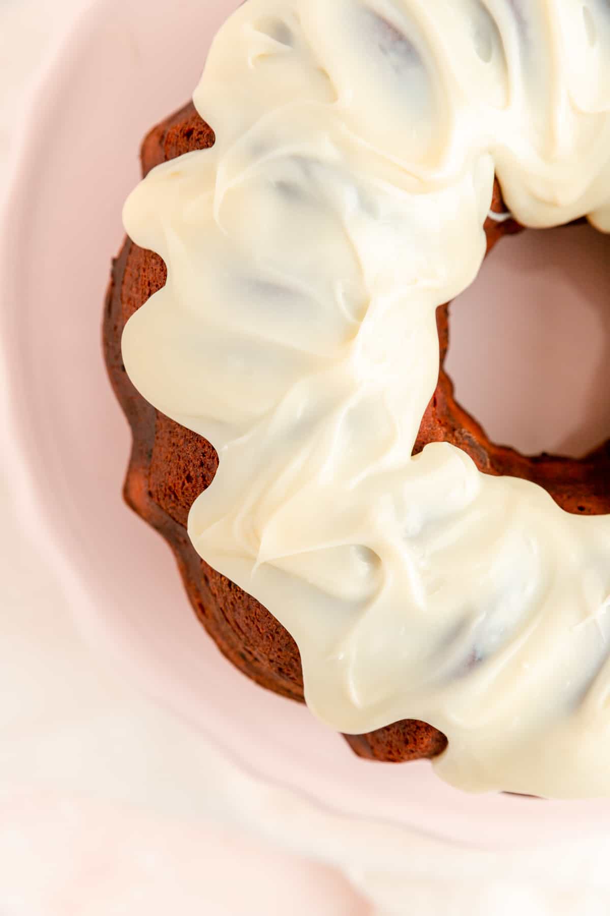 Close up overhead of white chocolate sauce and raspberry Bundt cake and pink cake plate.