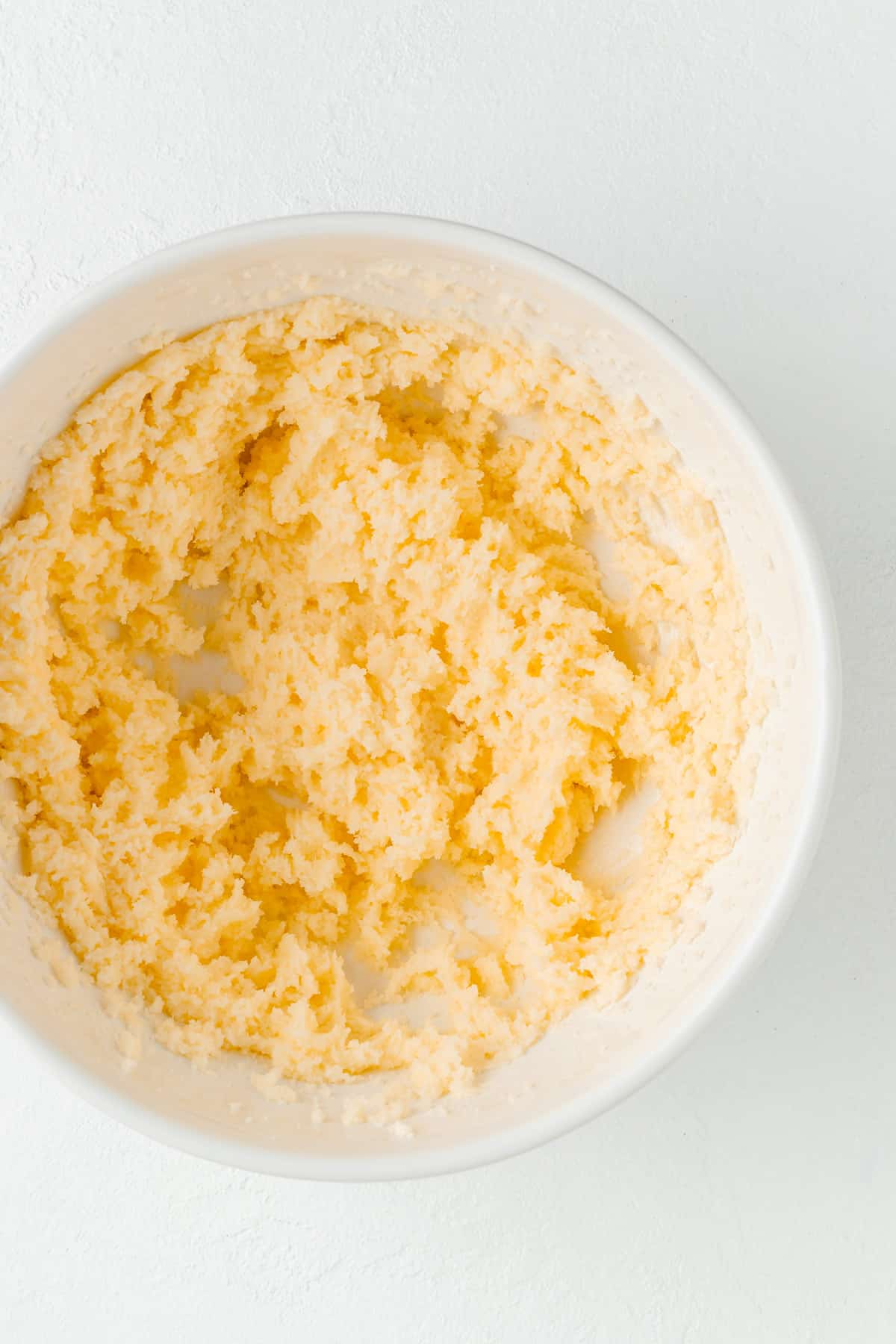Creamed butter and sugar in white mixing bowl on white background.