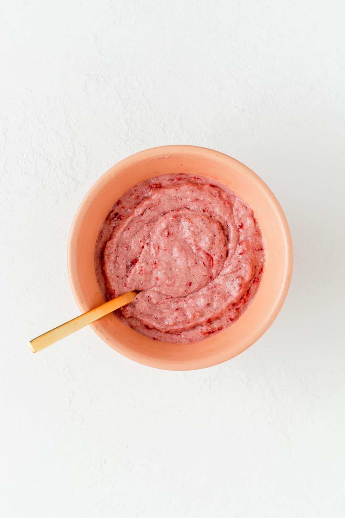 Raspberry layer batter in coral bowl with gold fork on white background.