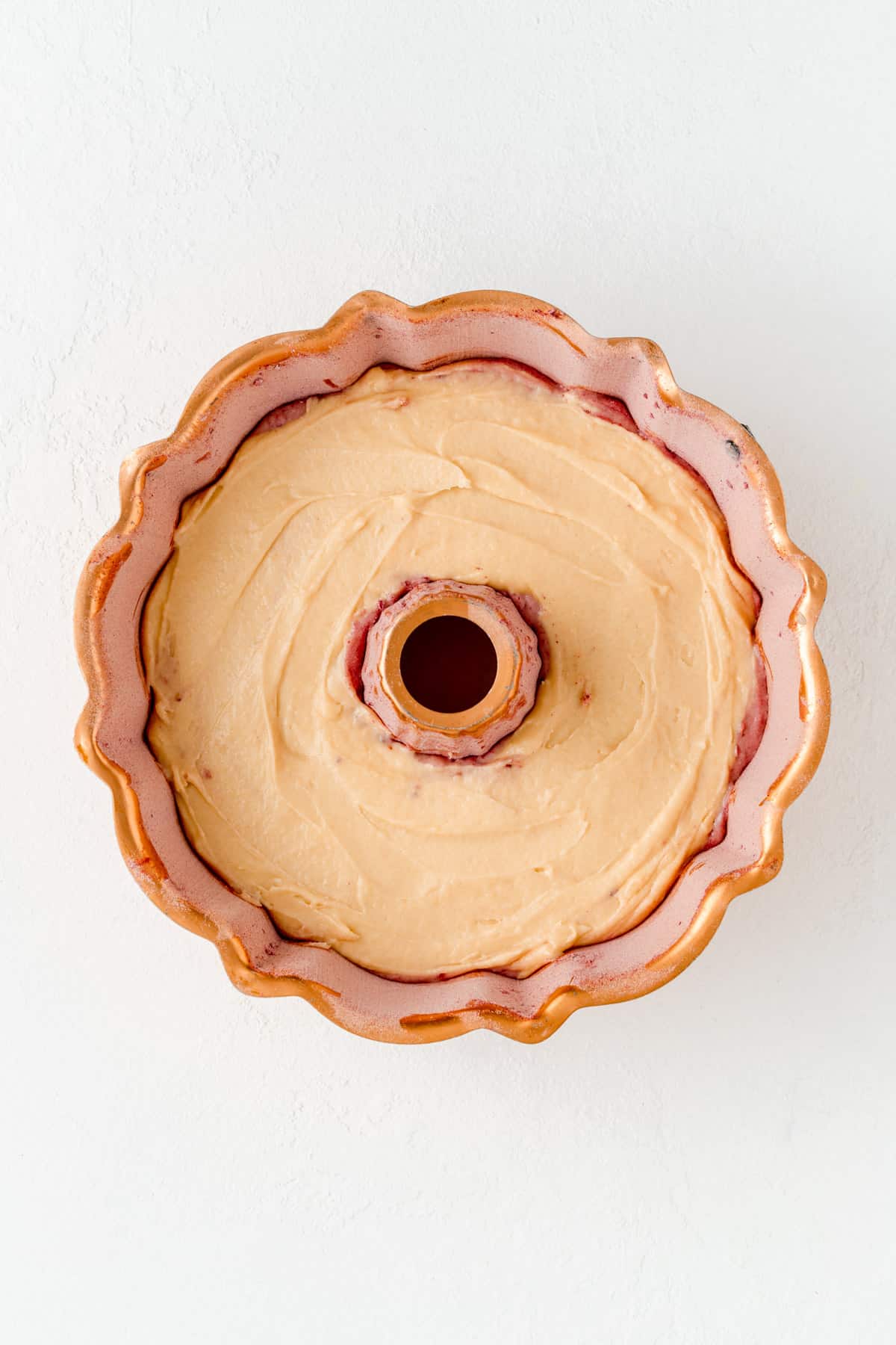 A copper Bundt pan with layered vanilla raspberry and then vanilla smooth batter on top.