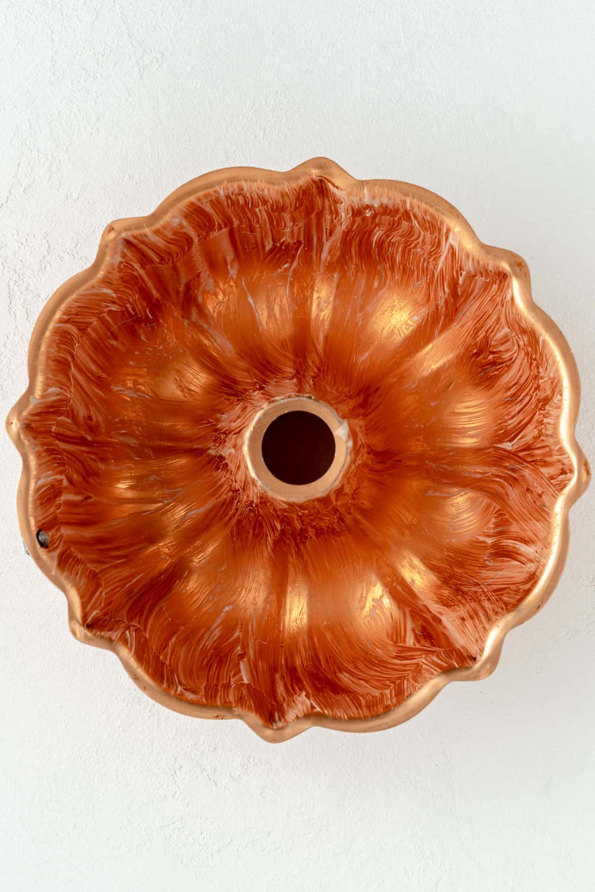 Copper Bundt pan brushed with melted butter on a white background.