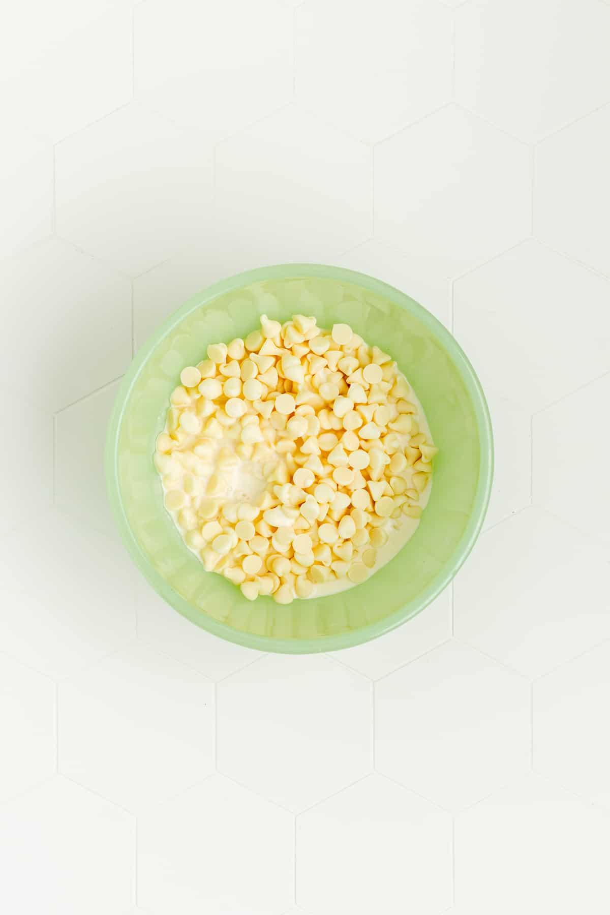 heavy cream and white chocolate chips in green glass bowl on white background.