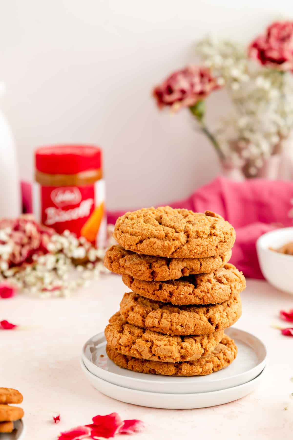 stack of six cookies on two plates with biscoff cookie butter container and flowers in background.