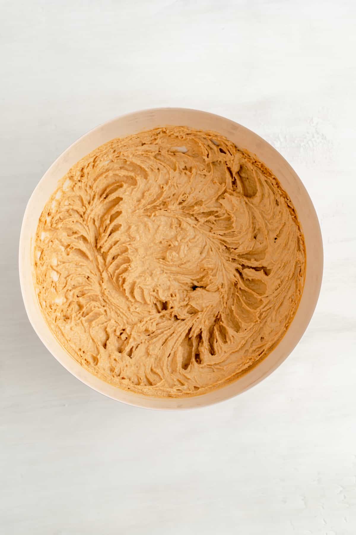 creamed butters, sugars, and egg in a tan mixing bowl on white wood background.