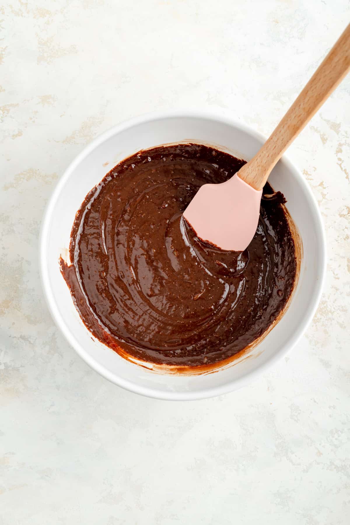 Final brownie batter in white mixing bowl with pink and would spatula.