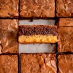 A close-up of square brownies with one on its side showing two layers.