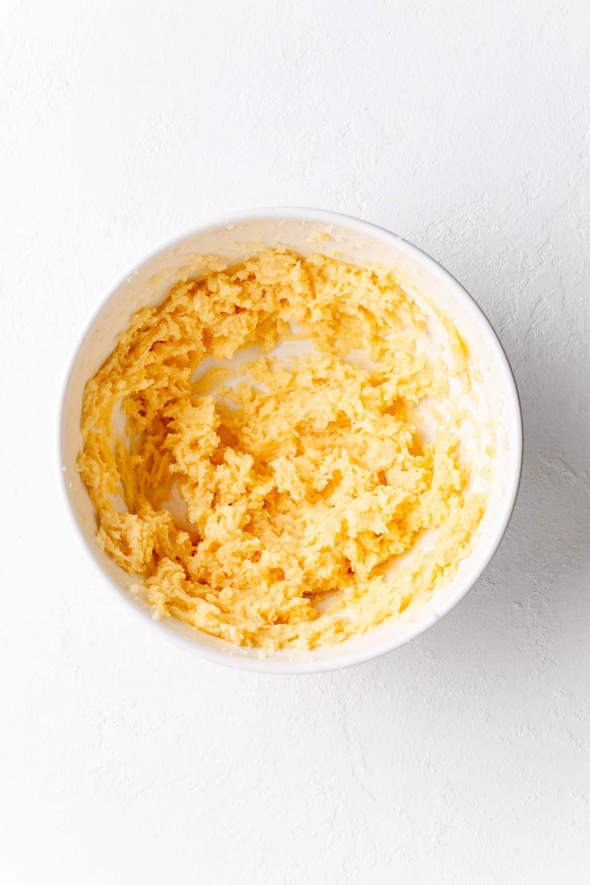 creamed butter, sugars and eggs in a white mixing bowl on a white background.