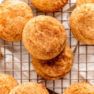 overhead shot of snickerdoodle cookies stacked on each other on a gold cooling rack.