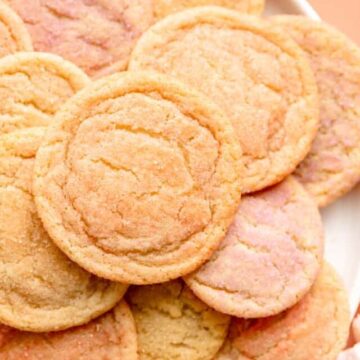 white plate piled with multi-colored sugar cookies on coral background with ranunculus on table.