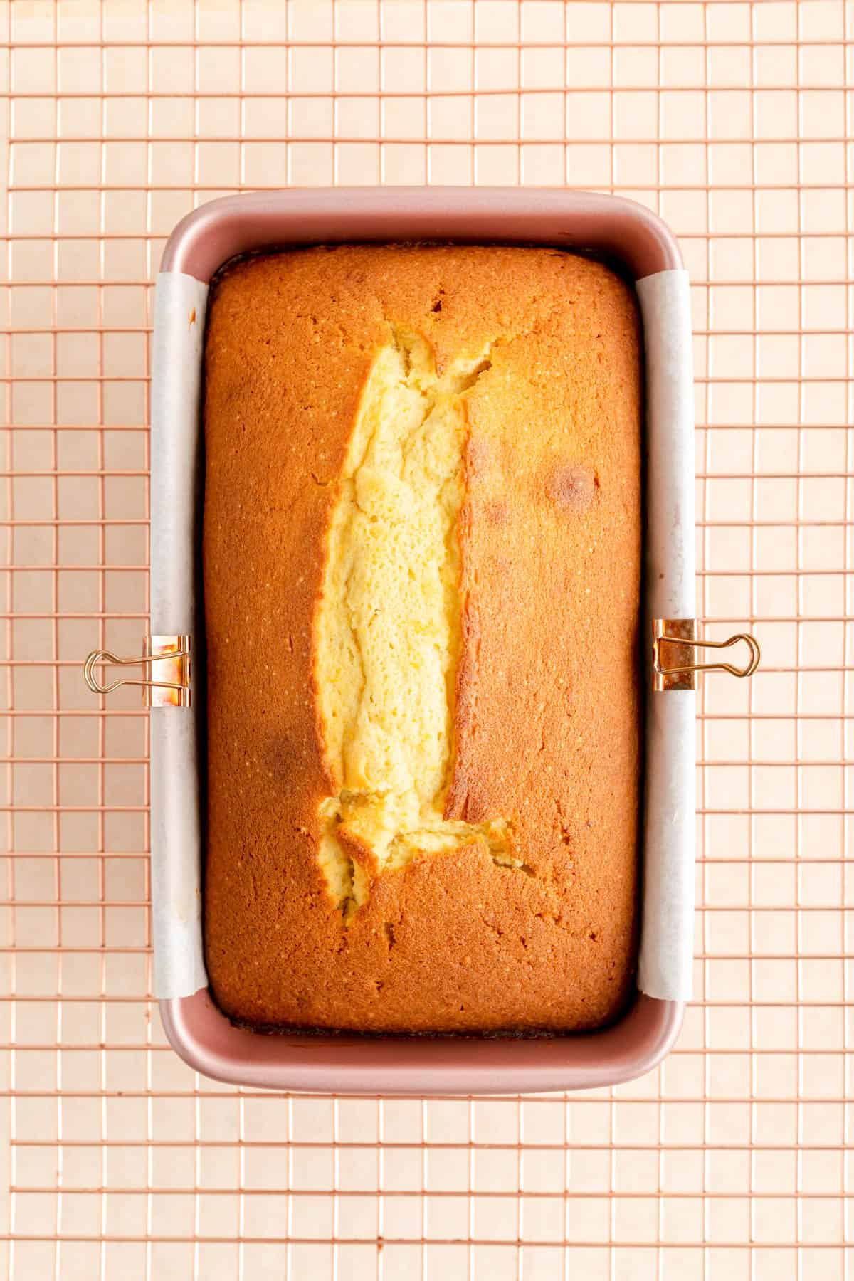 a fully baked citrus pound cake in a pink pan on a copper wire rack.