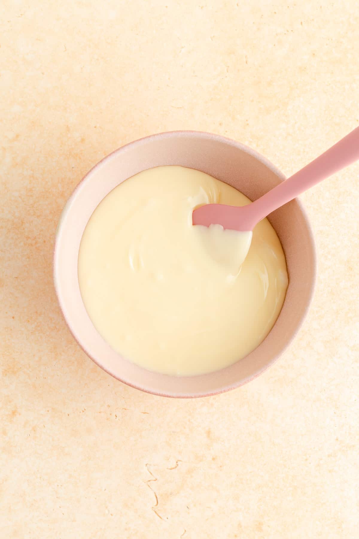 orange zest glaze in a pink bowl with a pink spatula on an orange background.