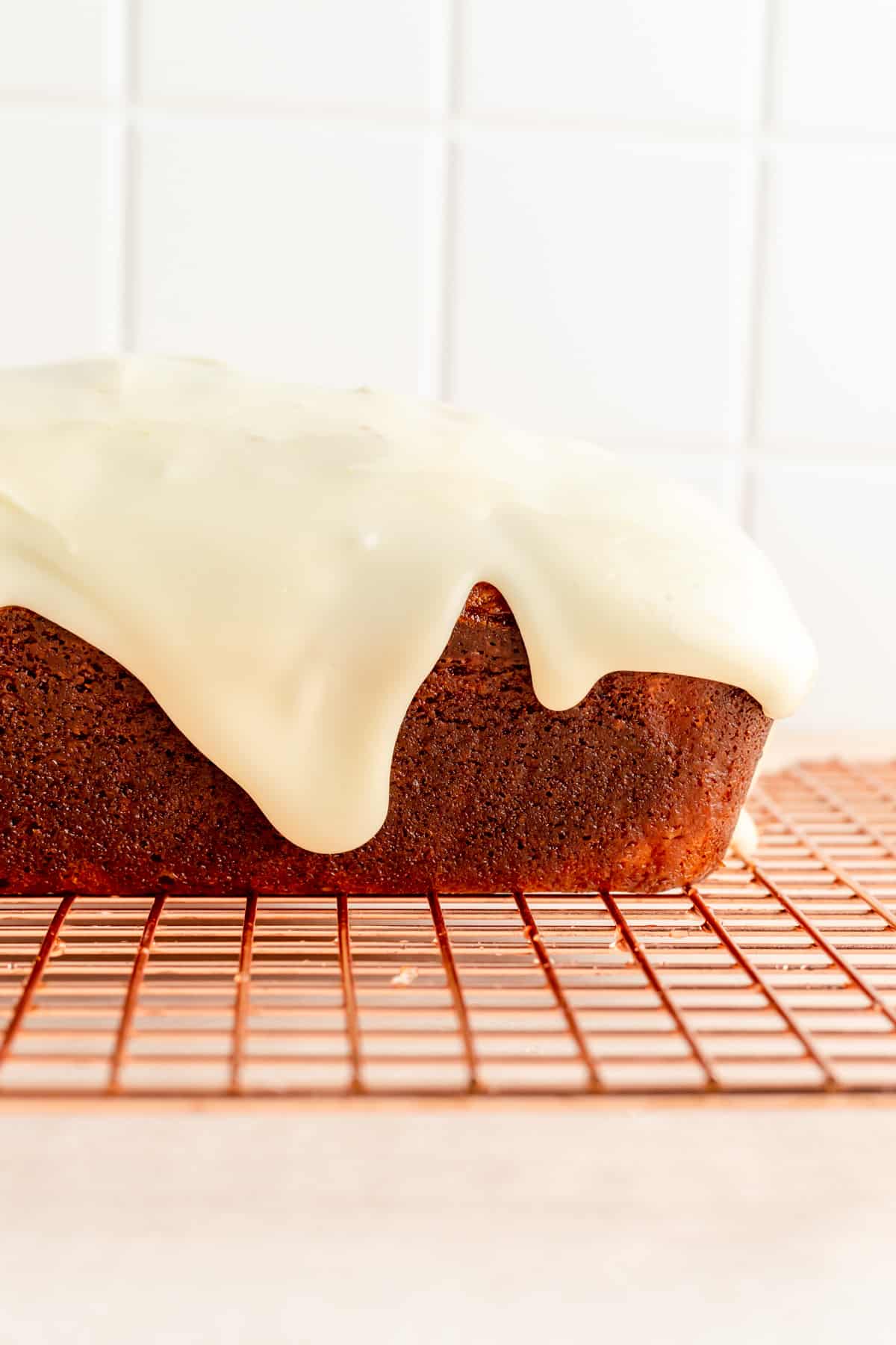 a side shot of glaze dripping off a pound cake on a copper rack.