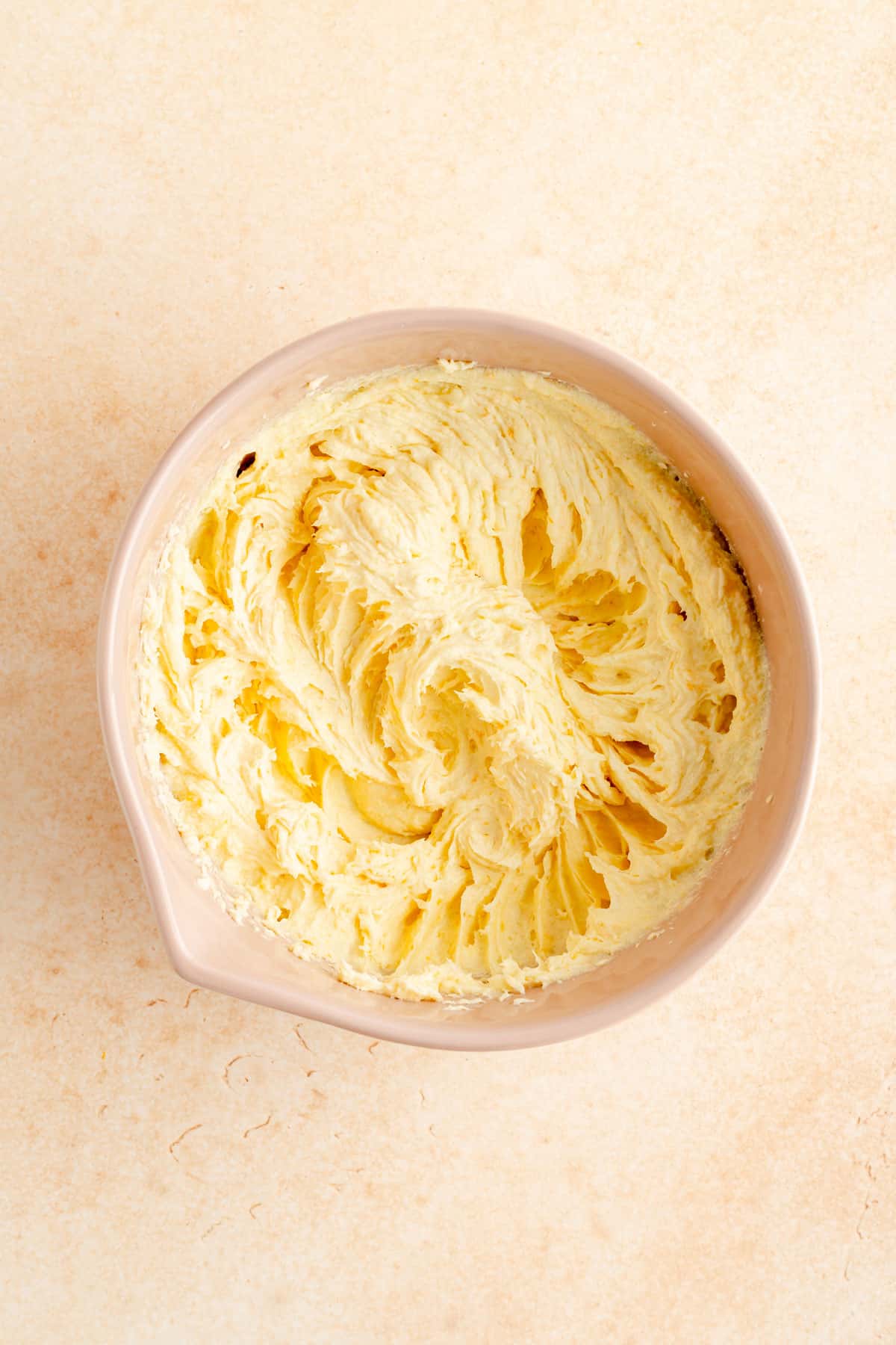 fats and sugar creamed in a tan mixing bowl on an orange background.