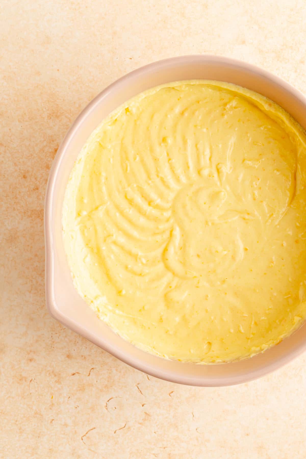 batter with fats, sugar, and eggs whipped in a tan bowl on an ornage background.