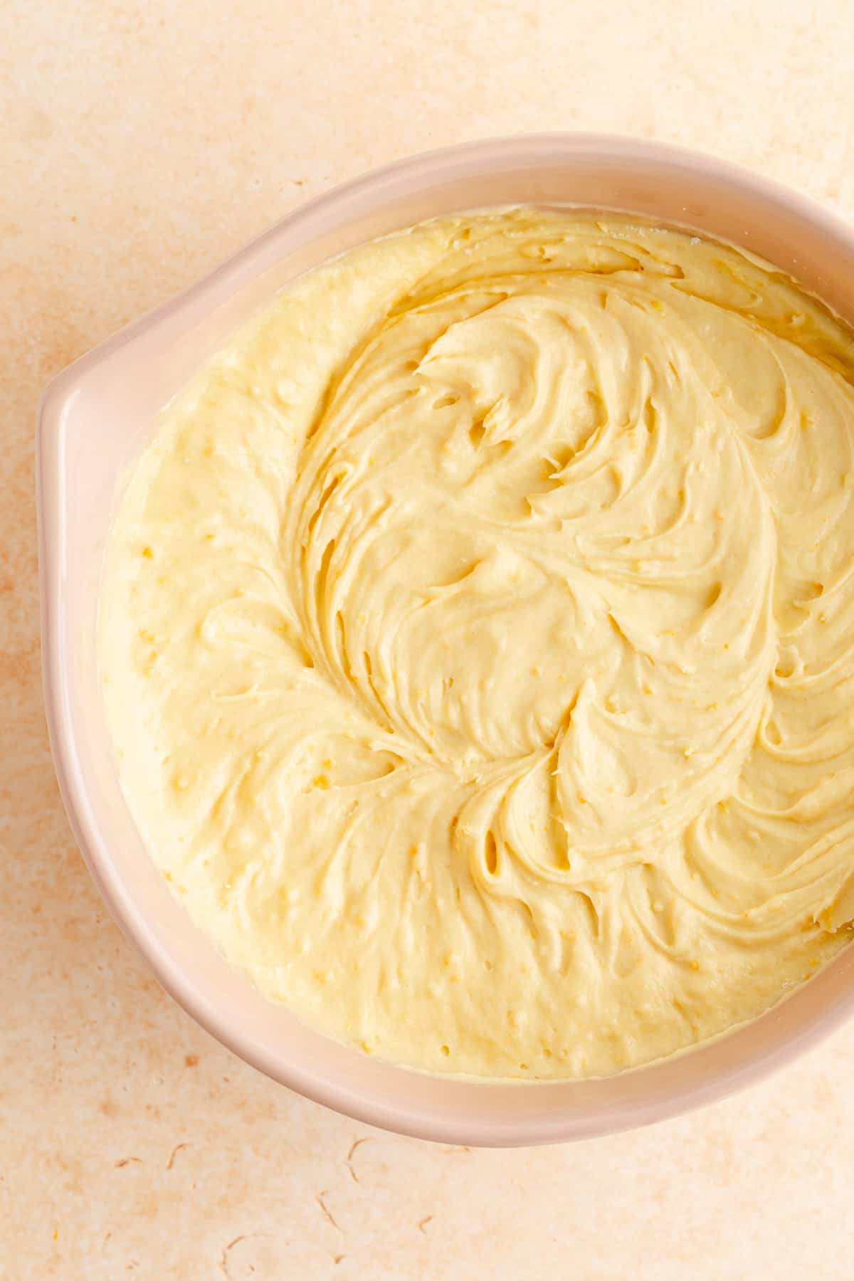 the final citrus pound cake batter in a tan mixing bowl on an ornage background.