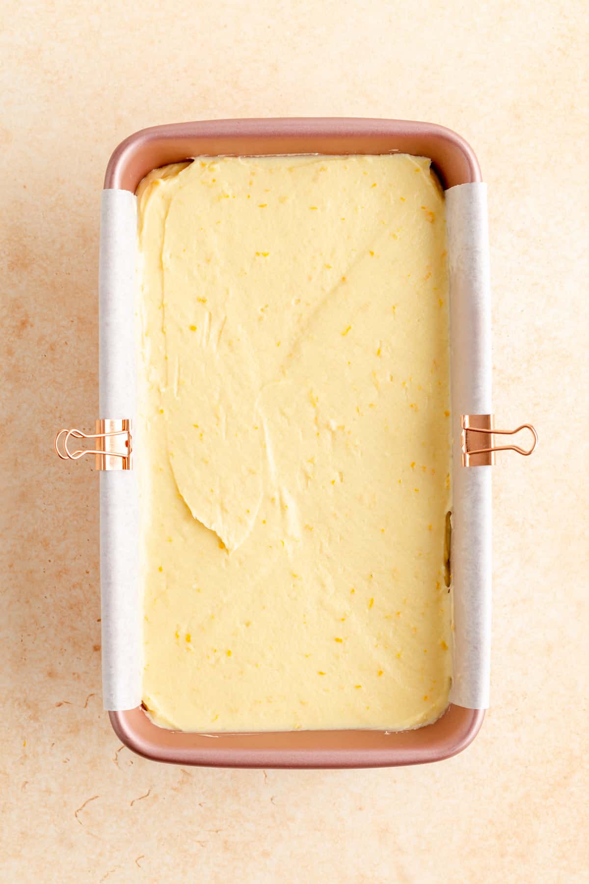 a pink parchment-lined baking pan filled with citrus pound cake batter on orange background.