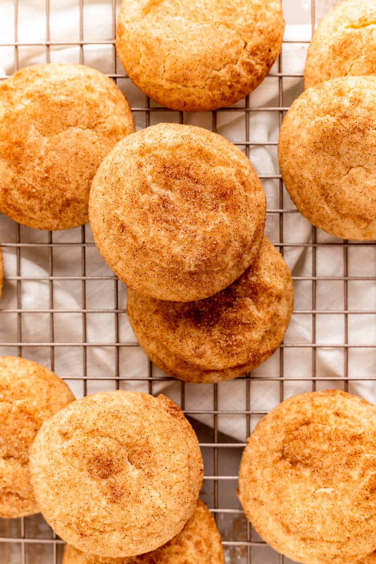 overhead shot of snickerdoodle cookies stacked on each other on a gold cooling rack.