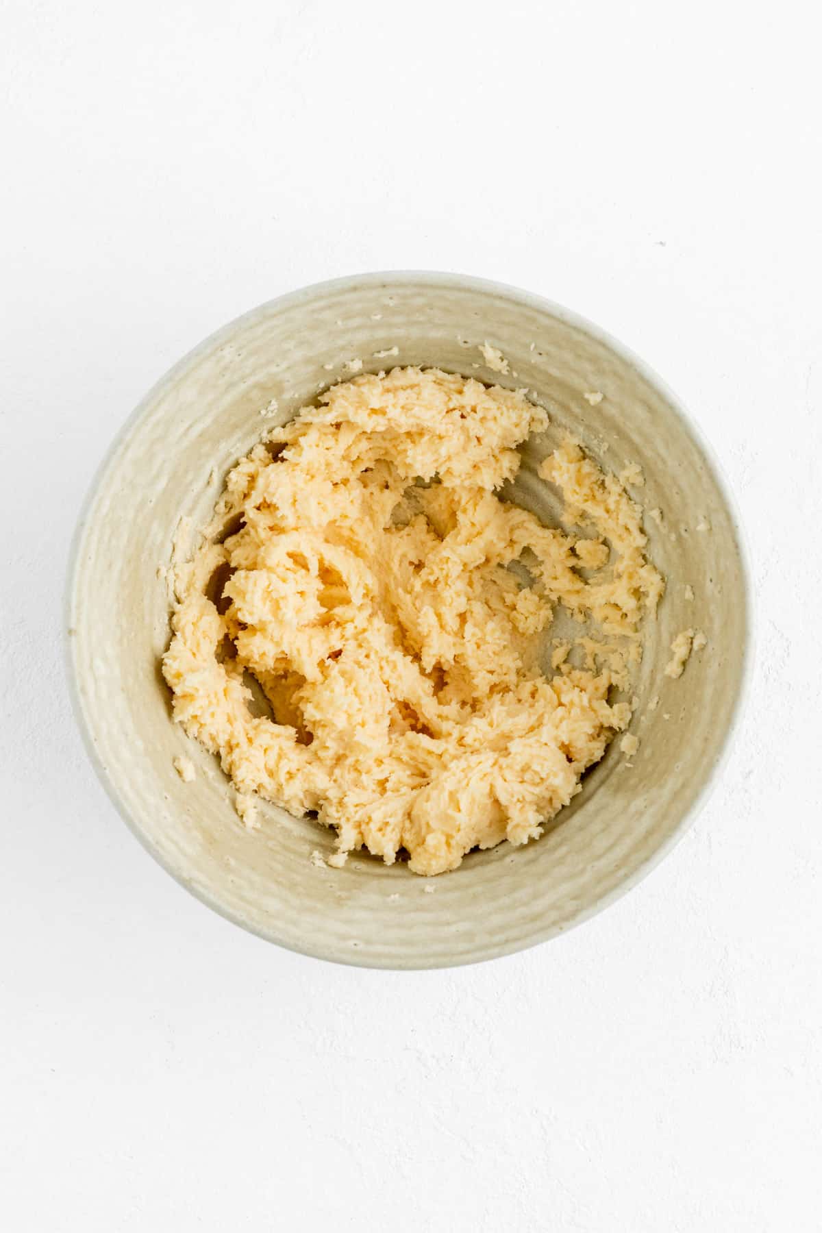 creamed butter sugar and eggs for cookie dough in a tan pottery bowl on white background.