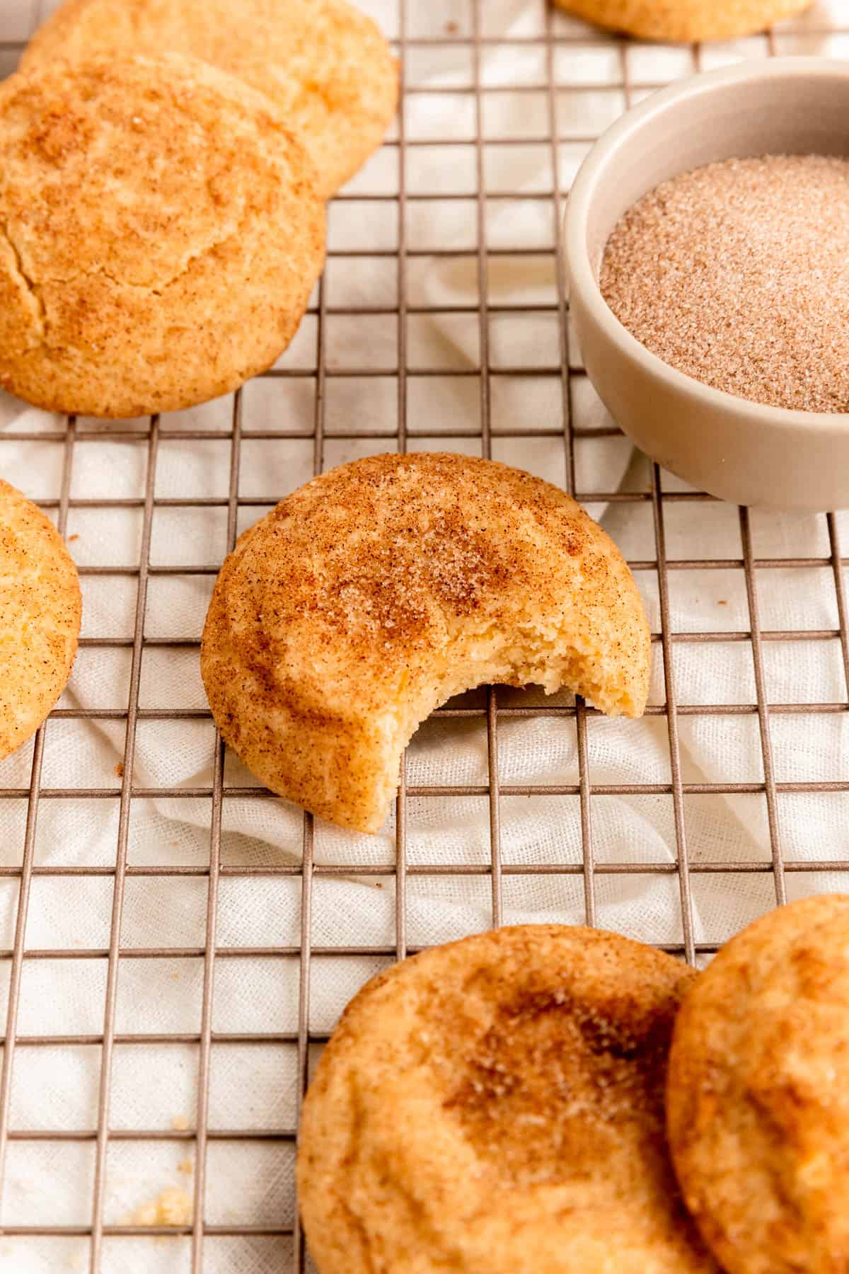 snickerdoodle cookie with bite out on gold cooling rack over white linen.