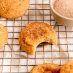 snickerdoodle cookie with bite out on gold cooling rack over white linen.