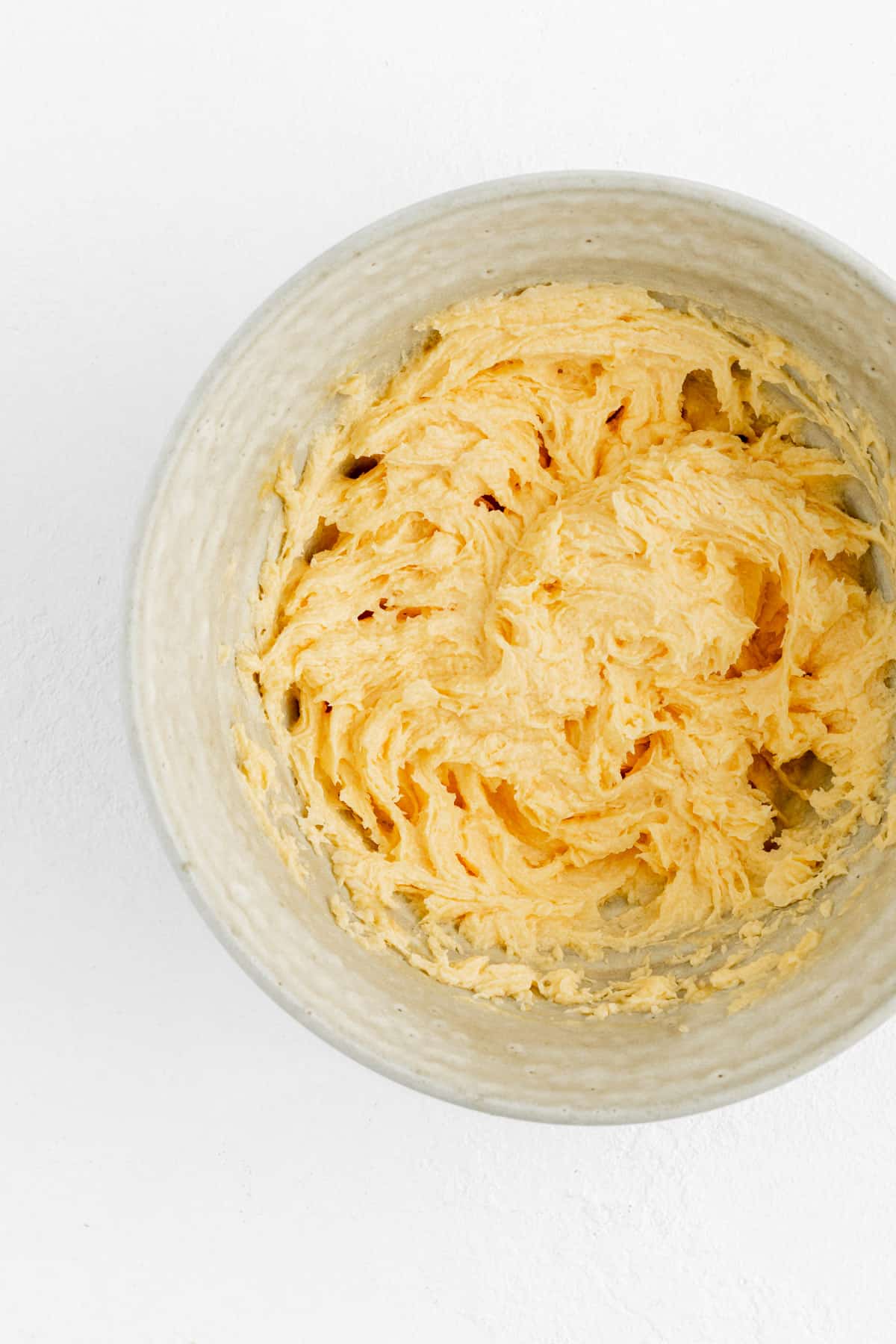 creamed butter sugar and eggs for cookie dough in a tan pottery bowl on white background.