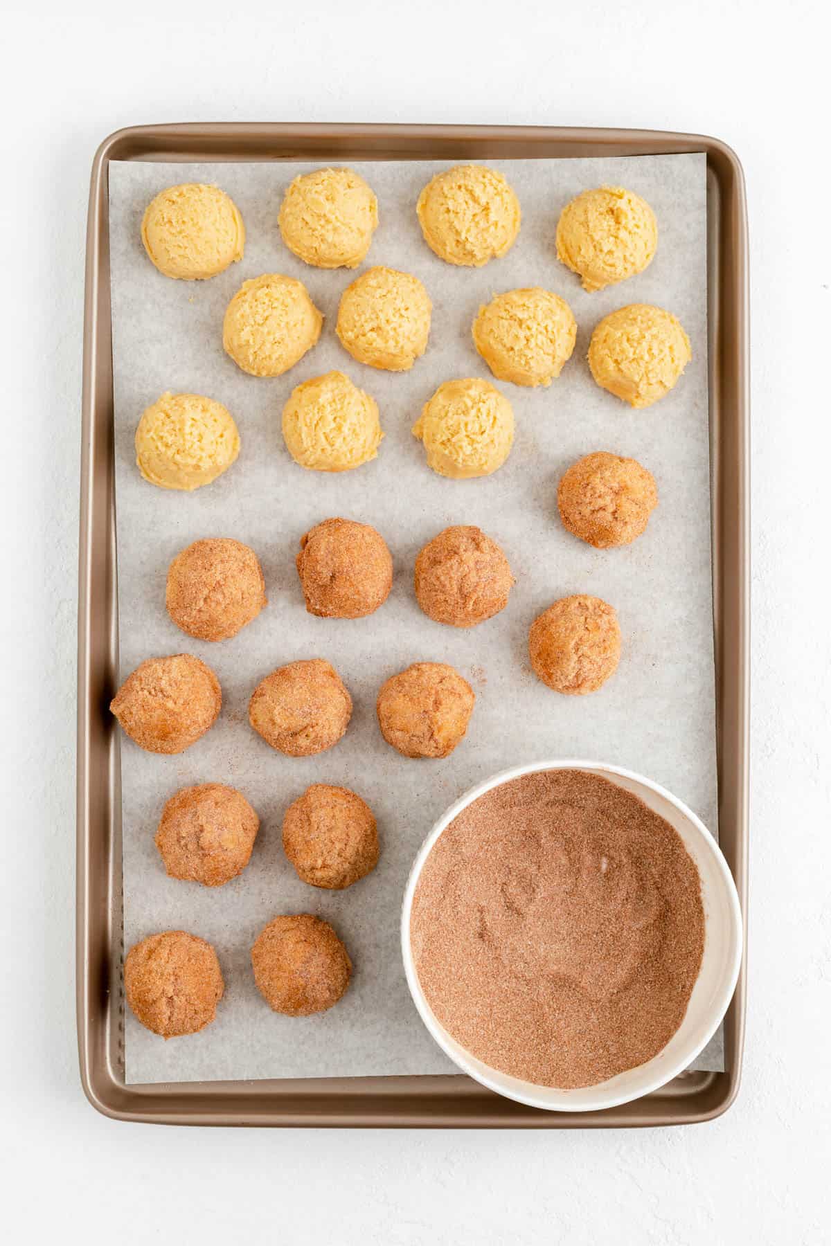 plain and cinnamon sugar coated snickerdoodle dough balls on a parchment lined gold baking sheet.