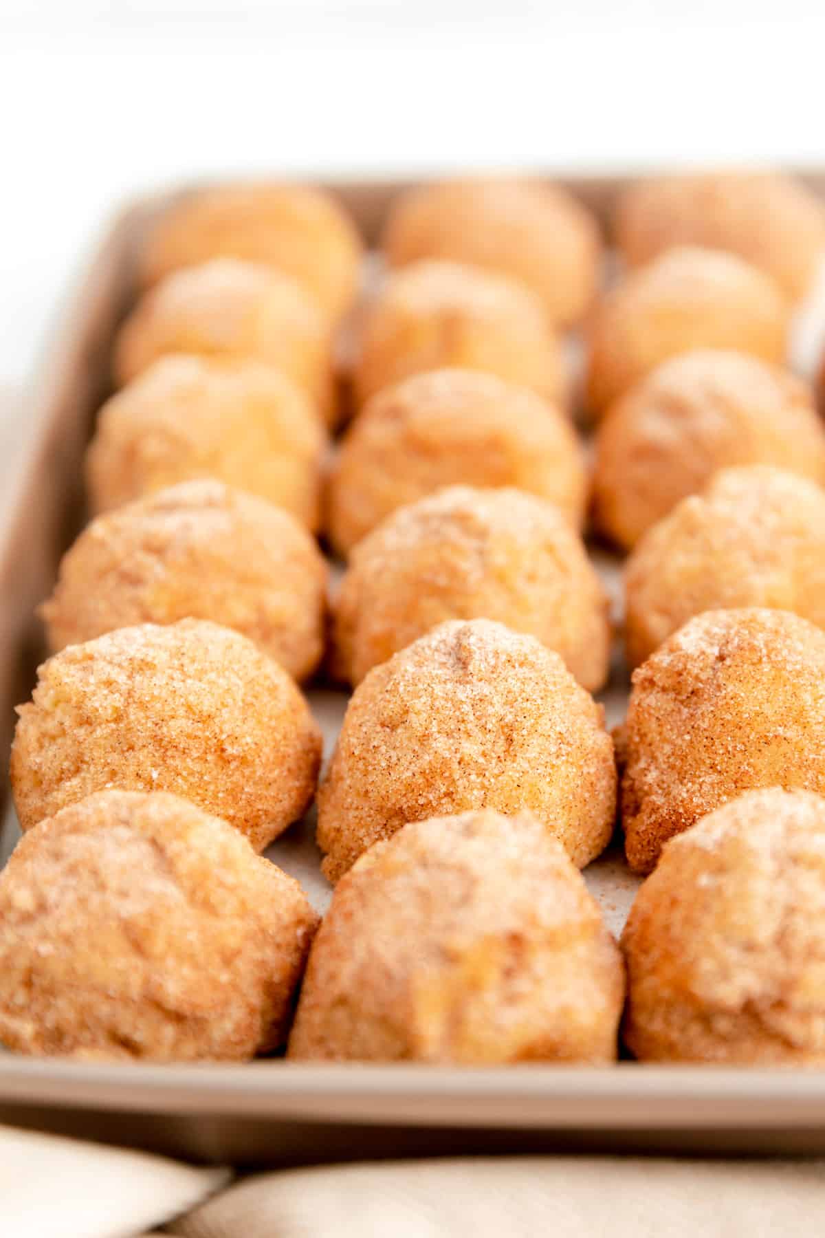 snickerdoodle dough balls lined up on a parchment lined gold baking sheet.