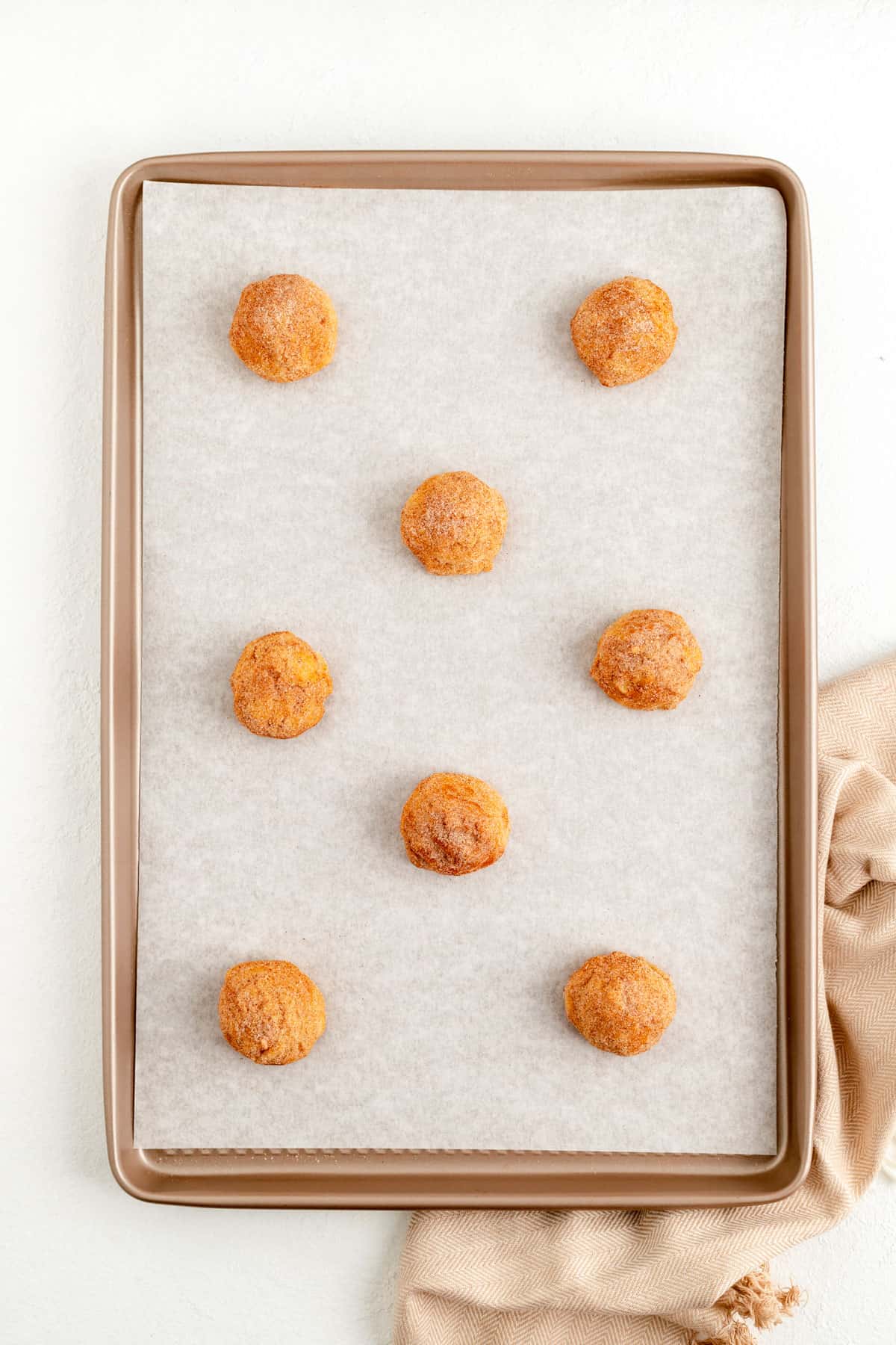 snickerdoodle dough balls spaced out on a parchment lined gold baking sheet.