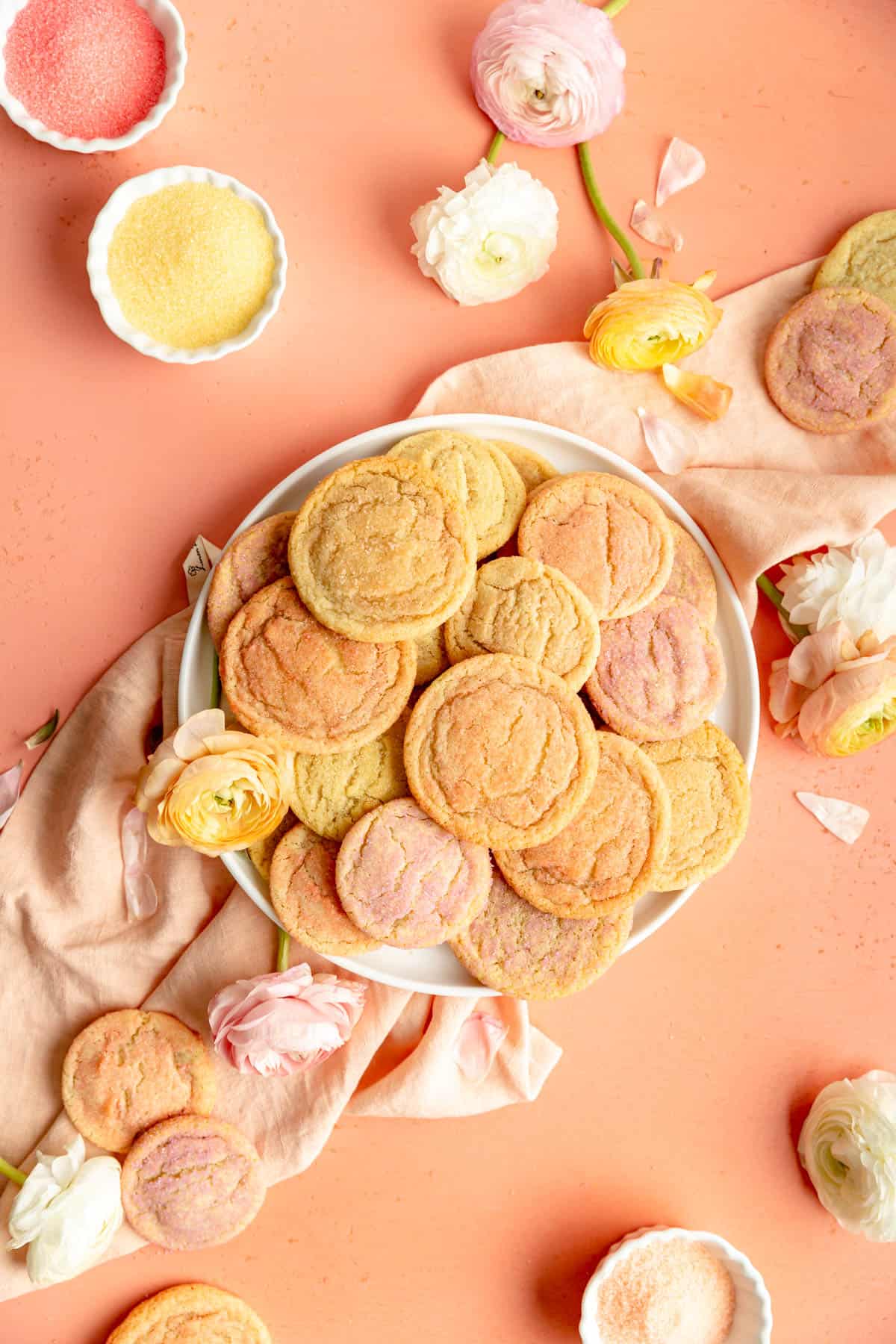 plate of orange yellow and pink sugar cookies on coral background with flowers and sugar bowls.