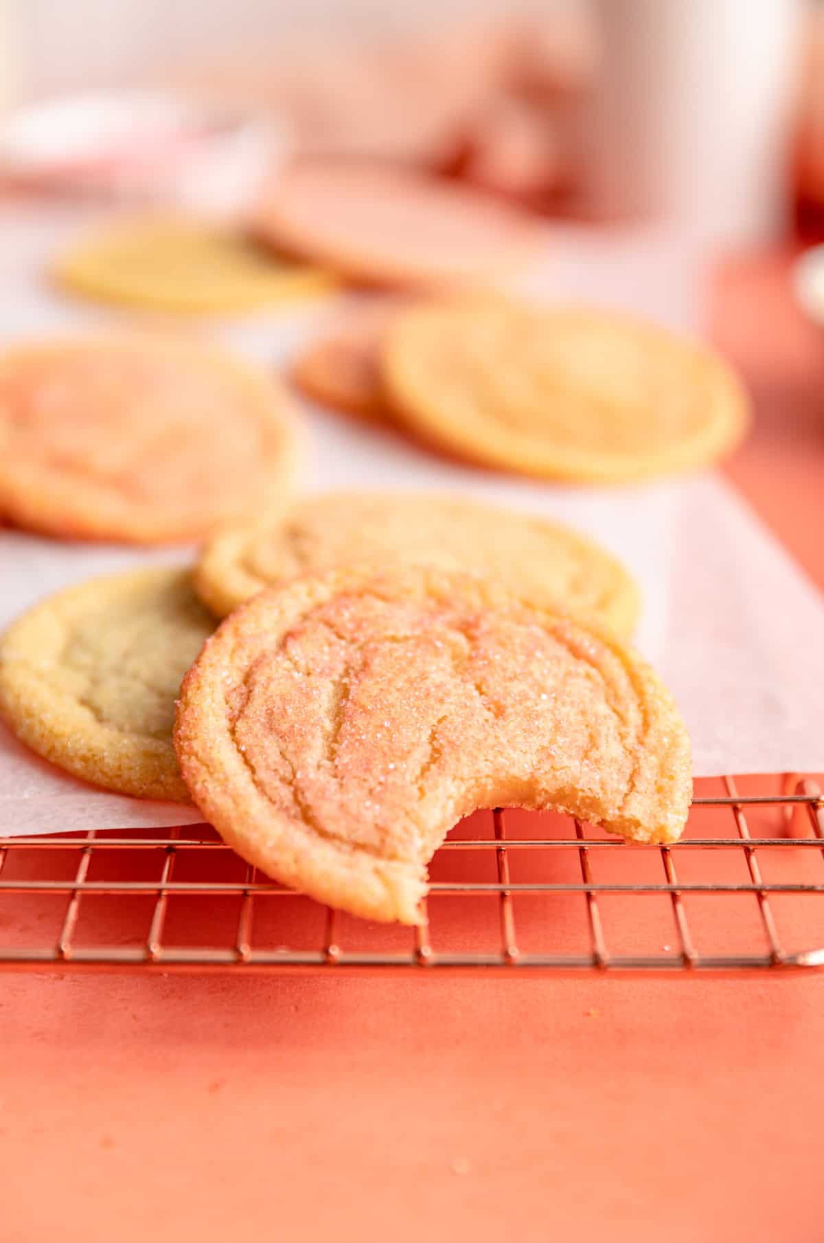 multi-colored sugar cookies on parchment and copper wire rack and front cookie with a bite out.