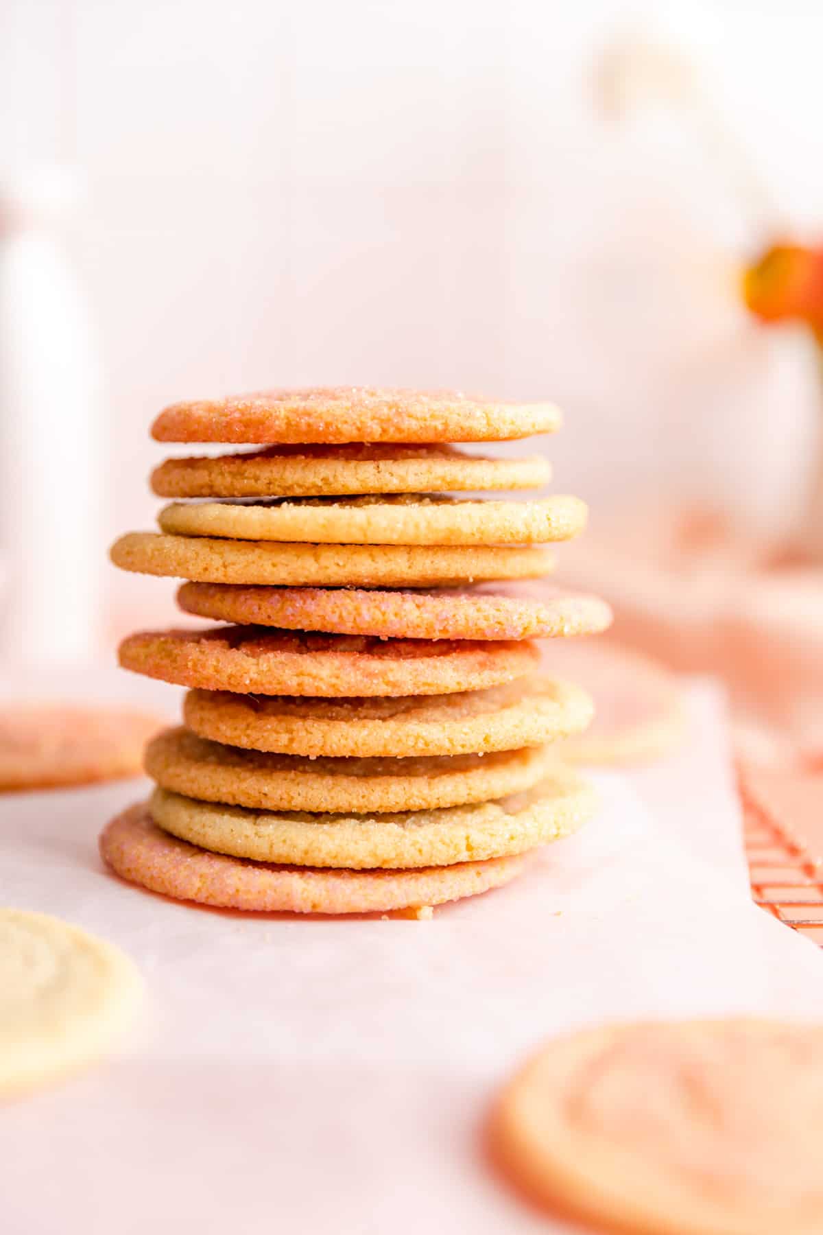 stack of pink orange and yellow sugar cookies on parchment with white background.