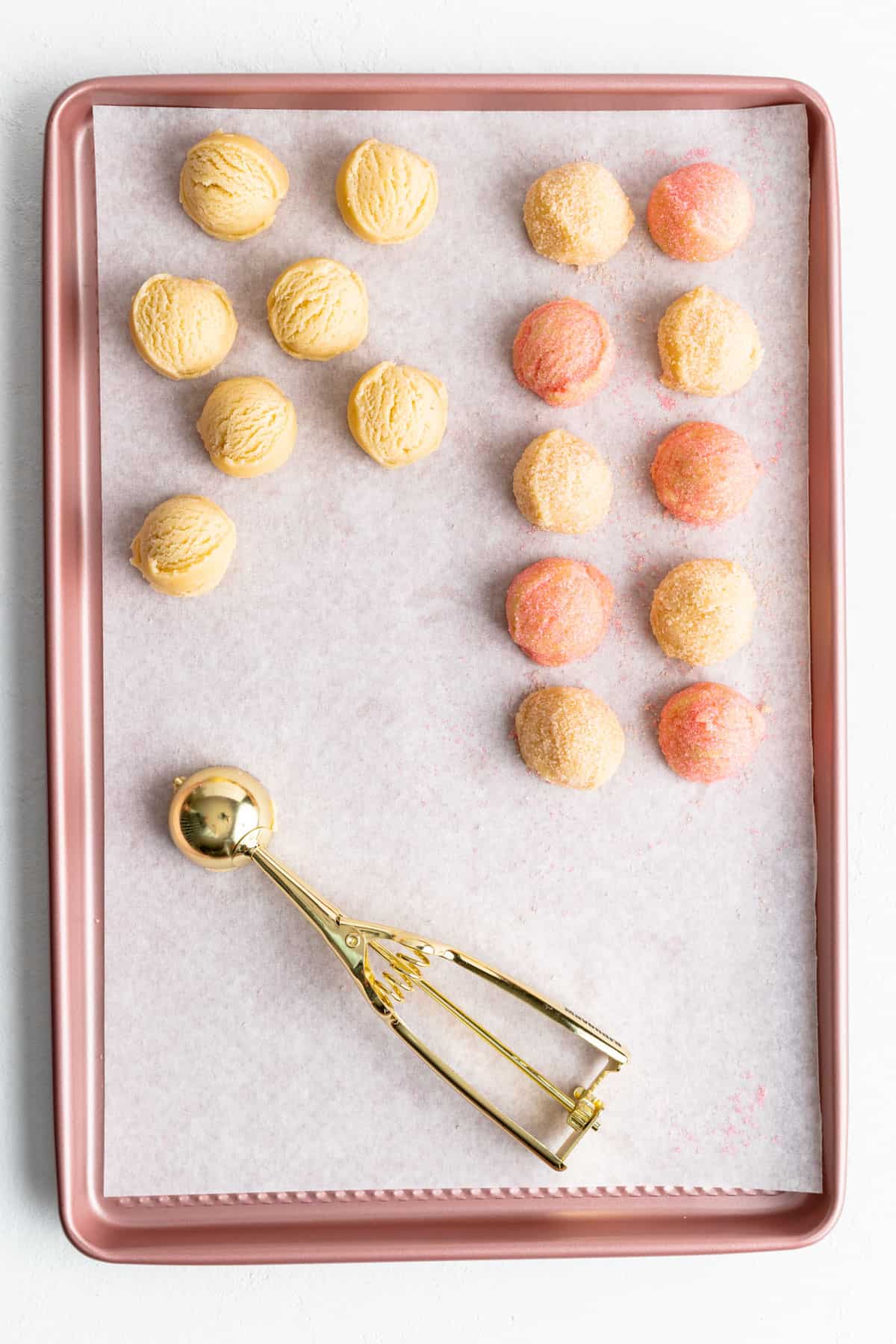 uncoated and orange and pink sugar coated dough balls on a pink parchment-lined baking sheet.