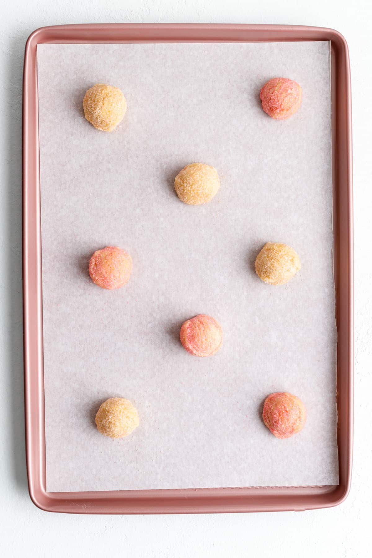 orange and pink sugar coated dough balls on a pink parchment-lined baking sheet.