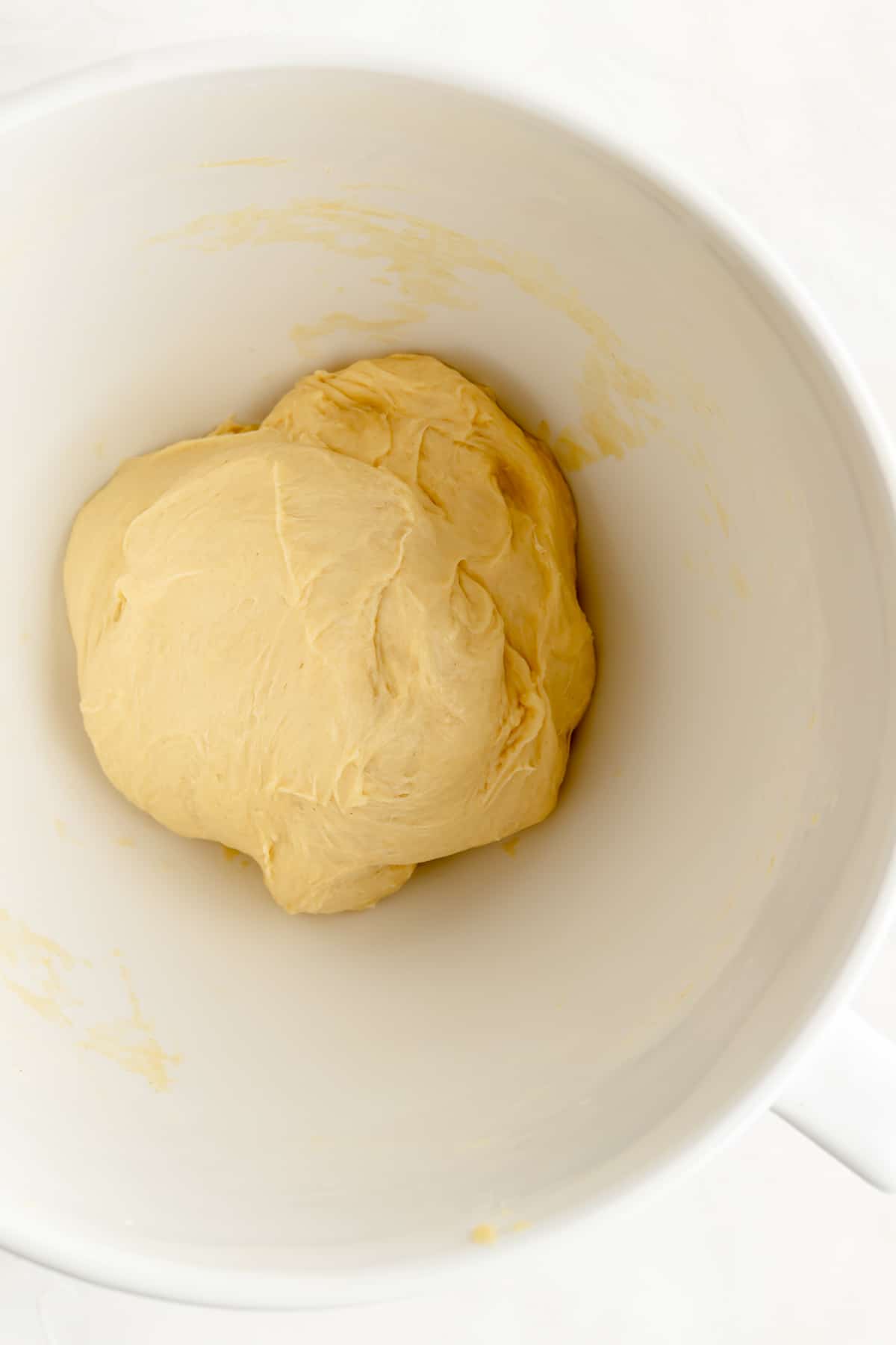 Partially developed ball of brioche dough in the bottom of a white bowl.