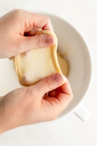 Two hands showing a piece of brioche dough in window pane structure over mixing bowl.