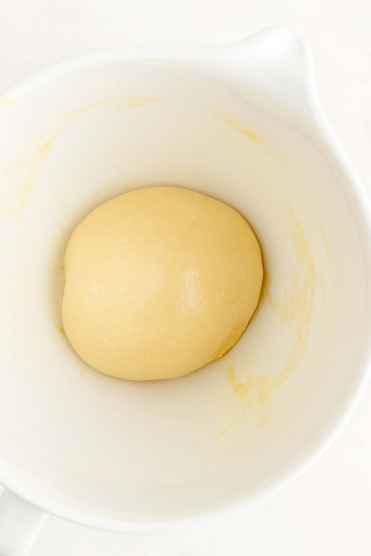 Un-risen greased ball of brioche dough in white bowl.