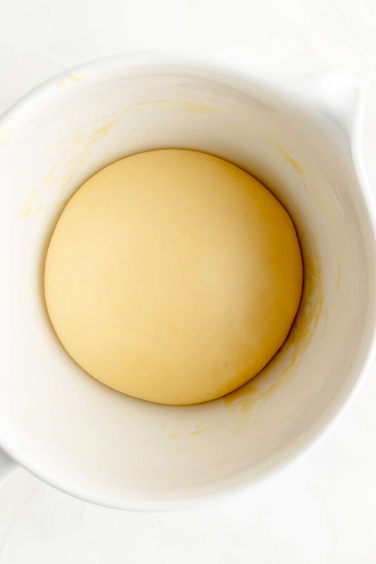 Risen ball of brioche dough in white bowl.