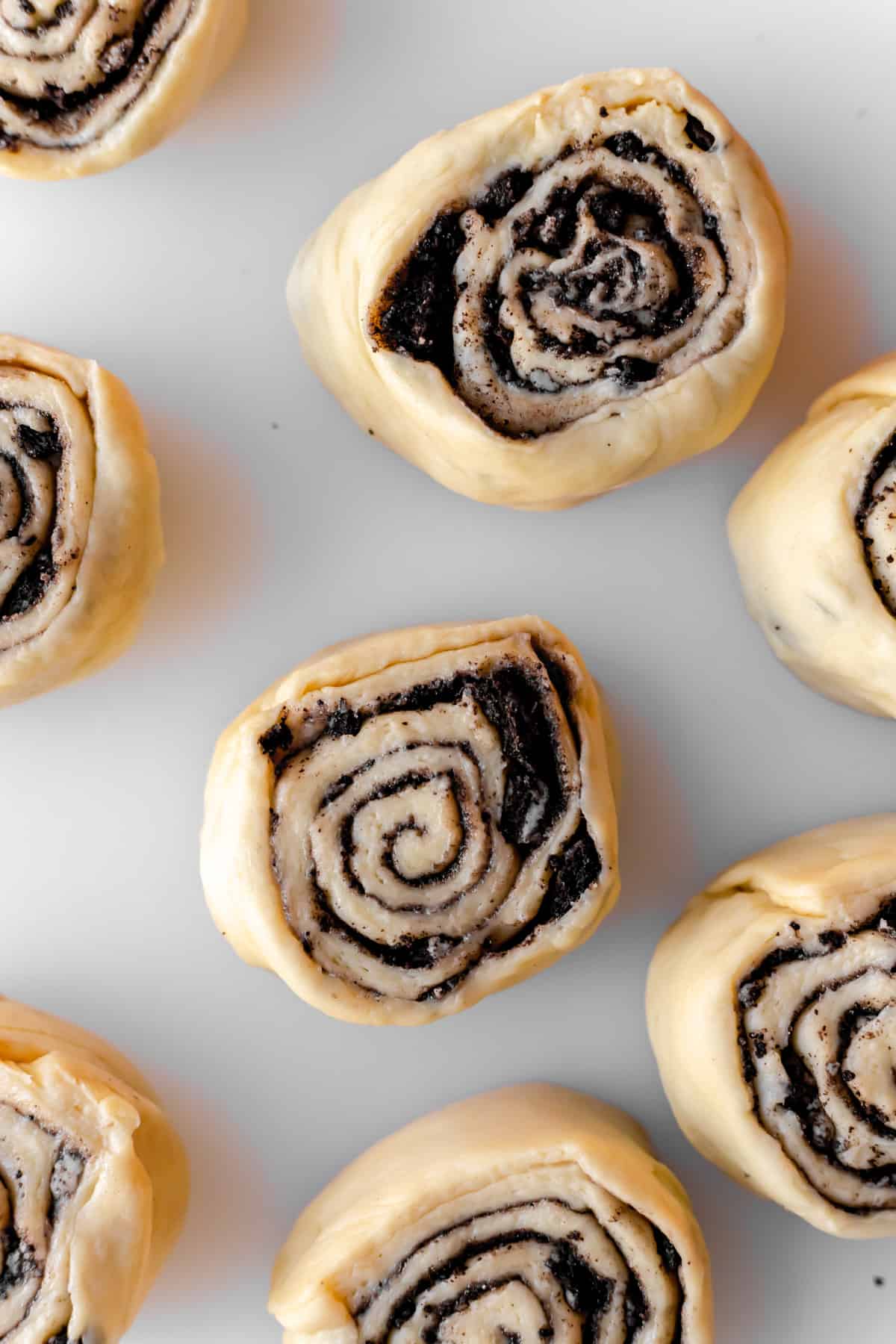 Overhead close-up of sliced cookies and cream cinnamon rolls on white cutting board.