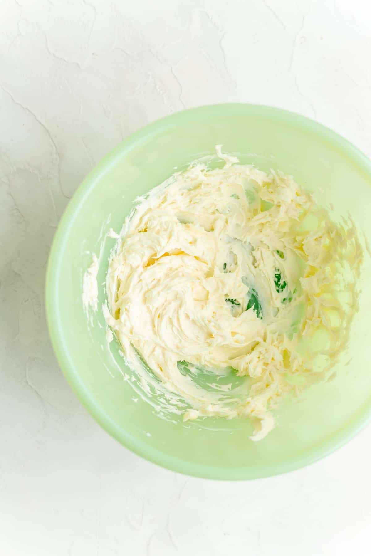 Whipped butter and cream cheese in green mixing bowl on white background.