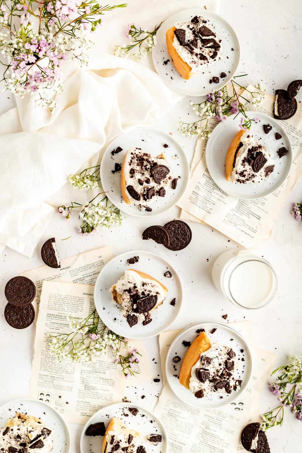 Lots of Oreo cinnamon rolls scattered on a table with recipe pages flowers and Oreos.