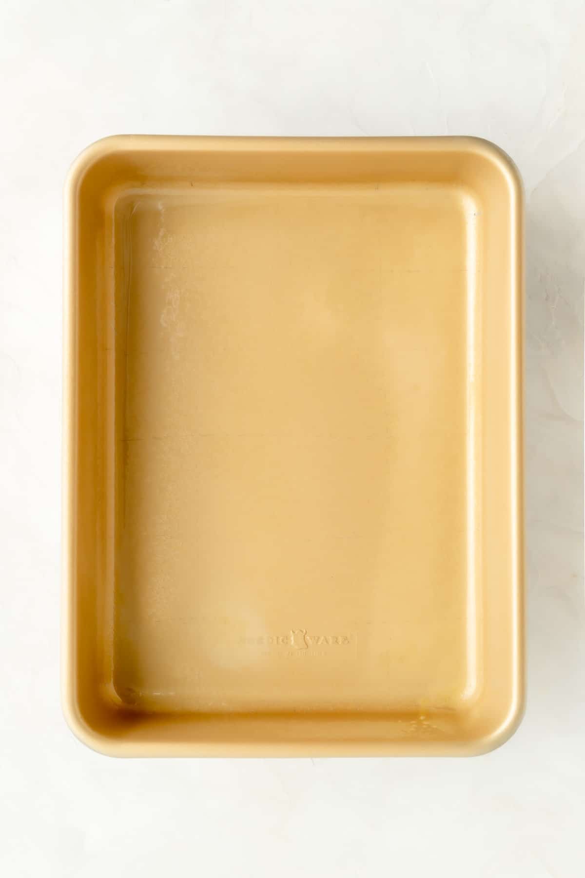 Greased gold 9 x 13 pan on a white background.