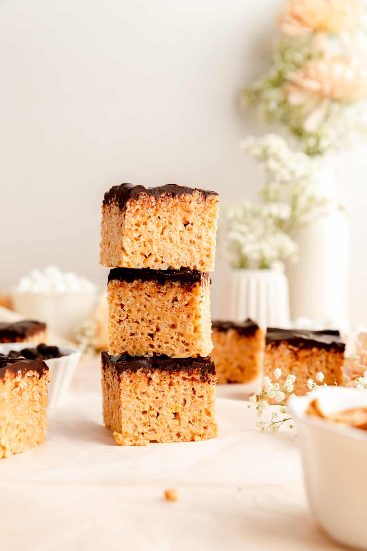 Stack of three rice krispie peanut butter bars with chocolate ganache and bars on table.