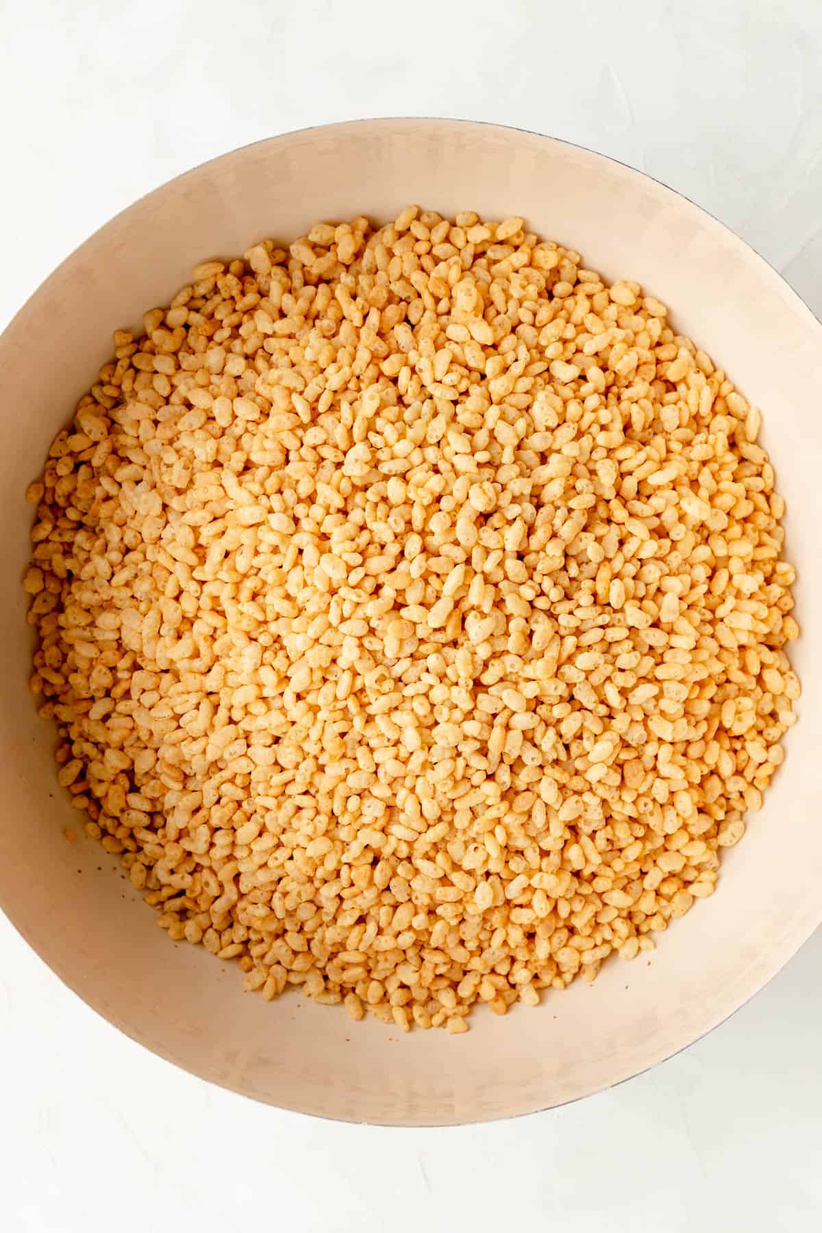 Large tan mixing bowl filled with rice crispy cereal on white background.