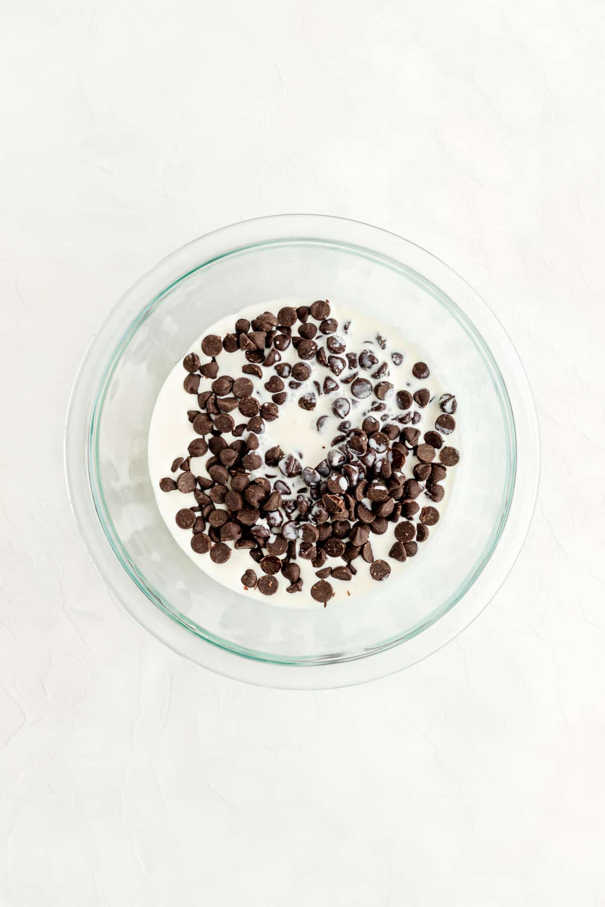 Dark chocolate chips and heavy cream in glass bowl and white background.