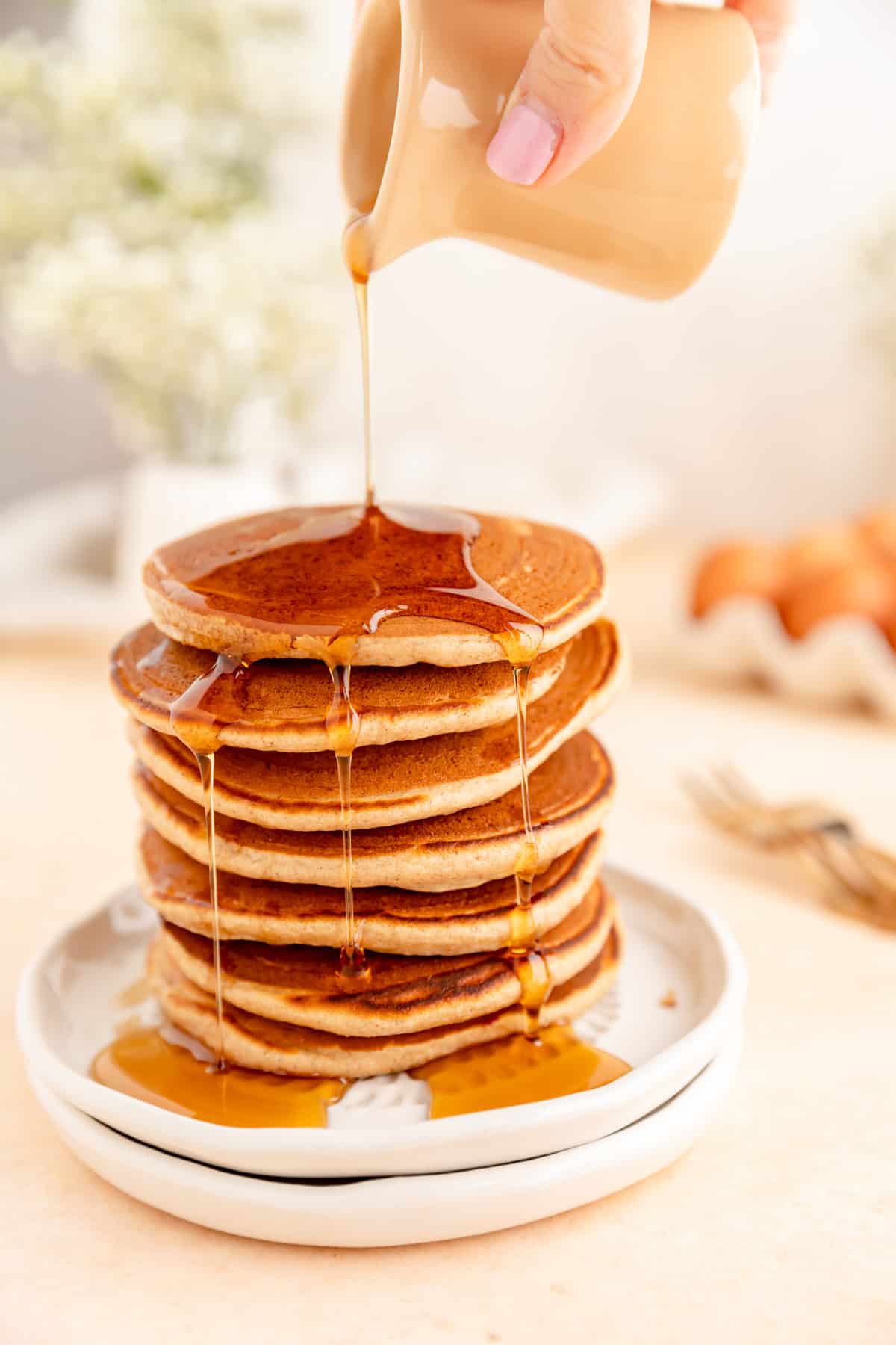 Close up of pancake stack with hand pouring lots of syrup down the side.