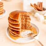 Side view of six pancakes stack with corner cut out and syrup dripping down.