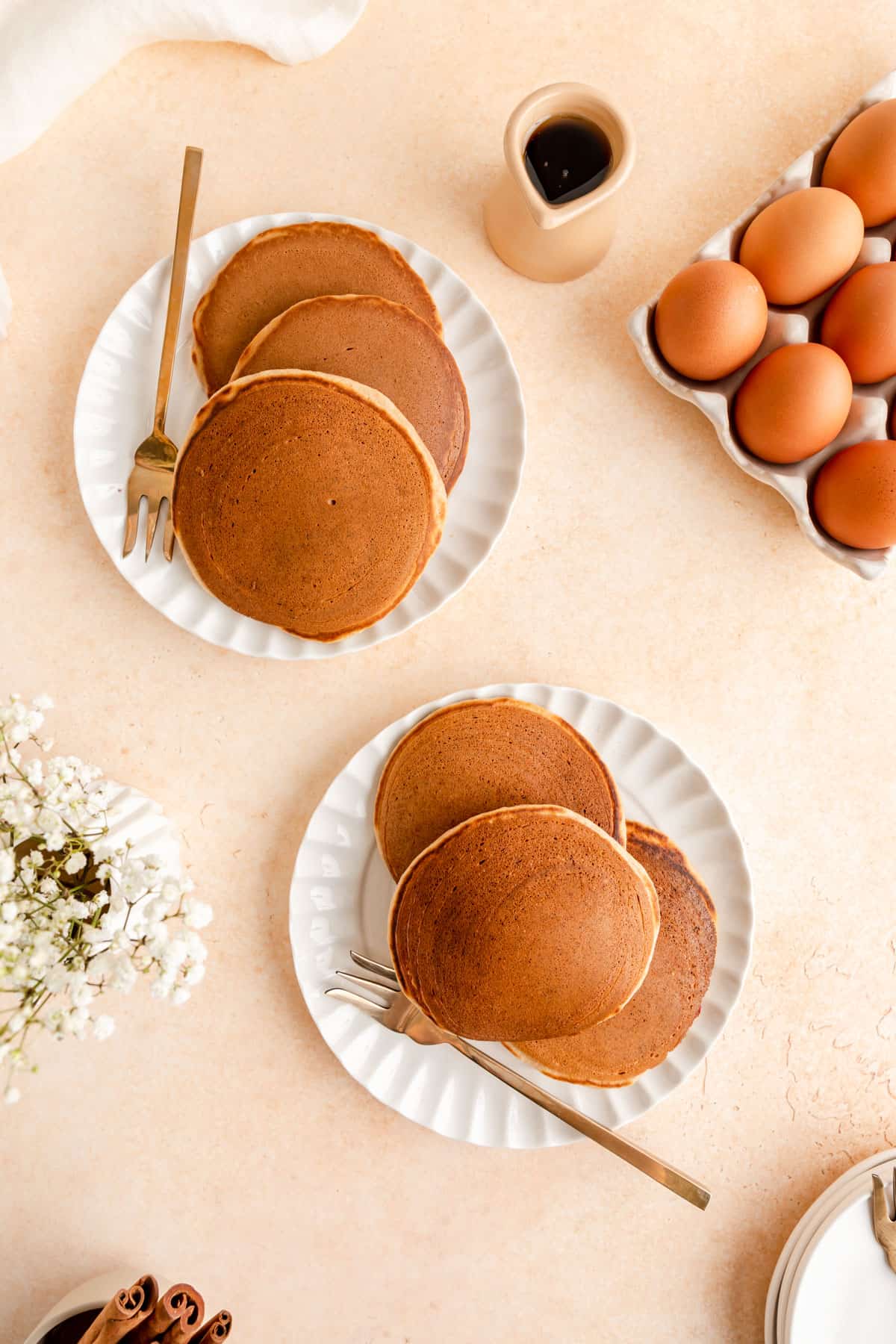 Overhead view of two plates of cinnamon pancakes with gold fork and egg tray..