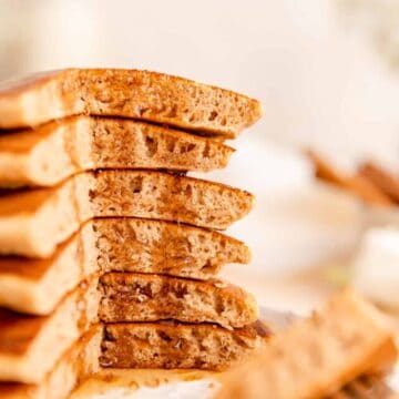 Close up side view of pancakes stack with a quarter cut out and syrup dripping down.