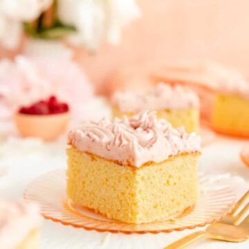 Square of vanilla cake with raspberry frosting on pink plate with gold fork.