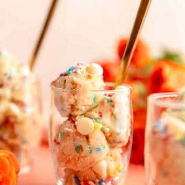 Three glasses with cookie dough scoops gold spoons and roses on the table.